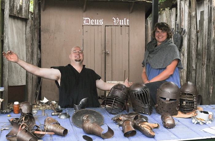 IHEA Armory volunteers smiling in front of a table displaying knight helmet and gauntlets at the Kansas City Renaissance Festival